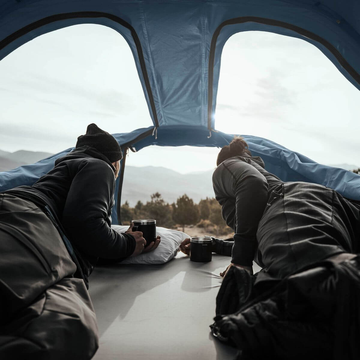 Two people relaxing inside Thule Approach - Car Roof Top Tents with scenic mountain view, showcasing Thule adventure gear.