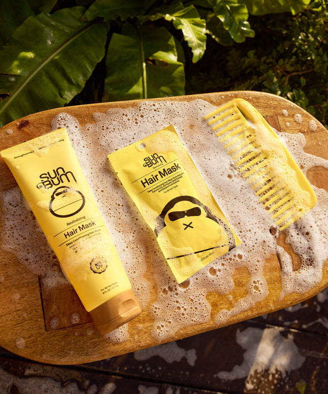Sun Bum Revitalizing Hair Mask with comb on a wooden surface surrounded by soap bubbles