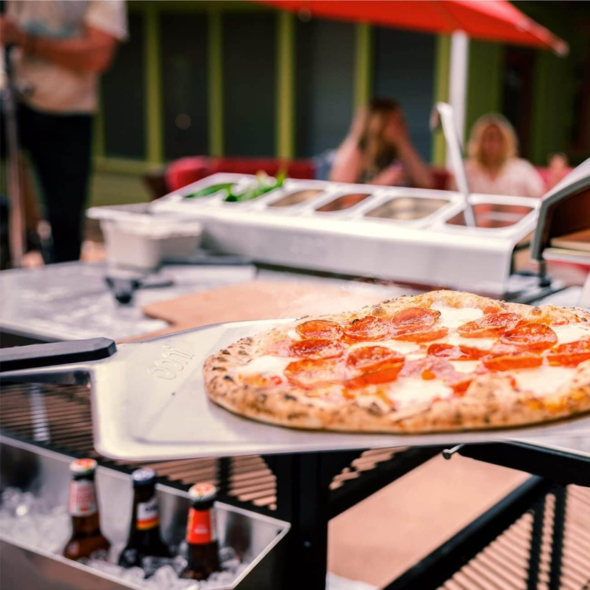 A delicious pepperoni pizza resting on an Ooni Pizza Peel at an outdoor gathering.