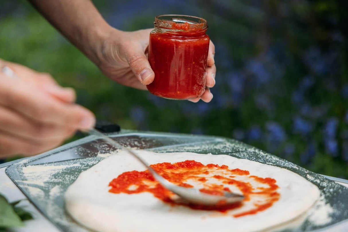 Applying tomato sauce to dough using Ooni Pizza Peel outdoors