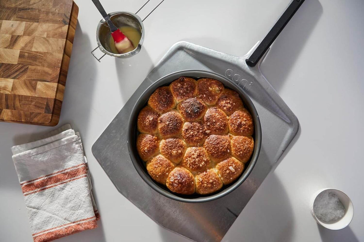 Ooni Pizza Peel holding freshly baked bread rolls, essential cooking gear for outdoor culinary experiences.
