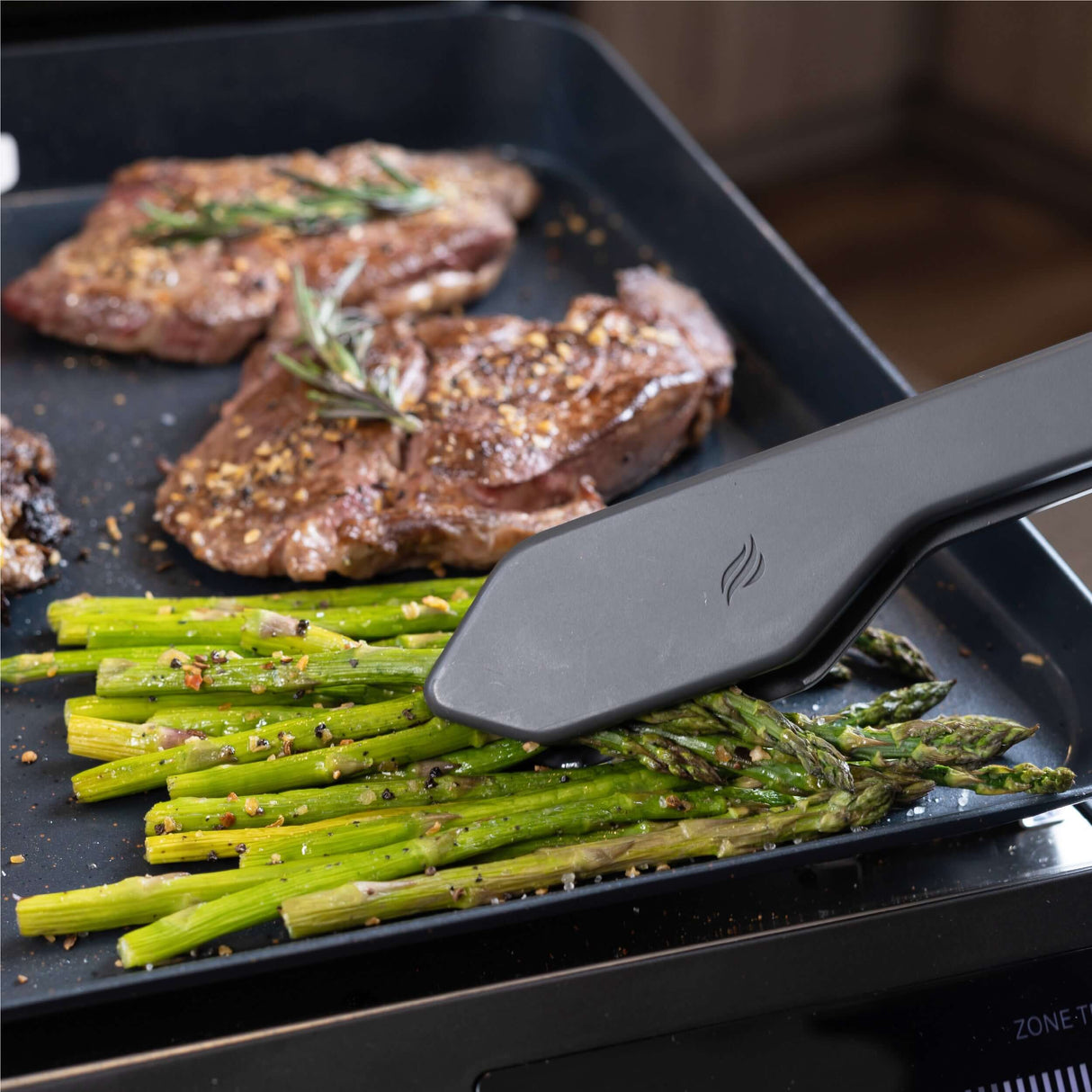 Cooking asparagus and steaks on Blackstone E-Series Electric Tabletop Griddle - 17 Inch with digital control.