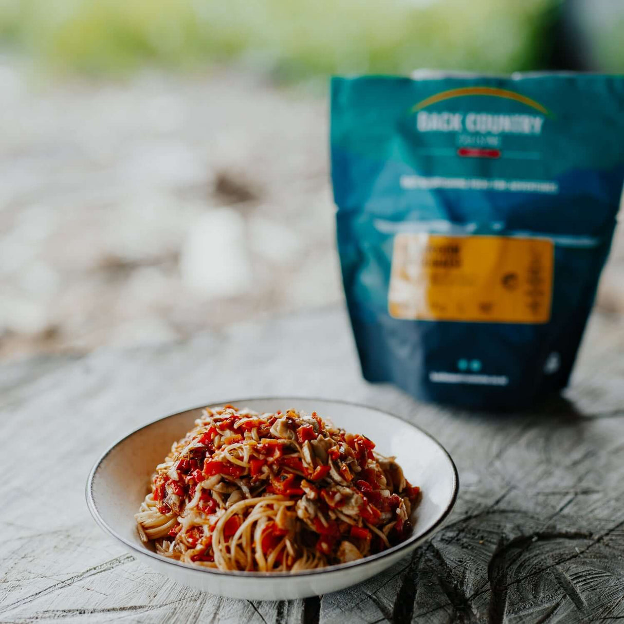 Back Country Cuisine Mushroom Bolognaise pasta meal on a rustic table, packaged for outdoor adventures and quick home meals.