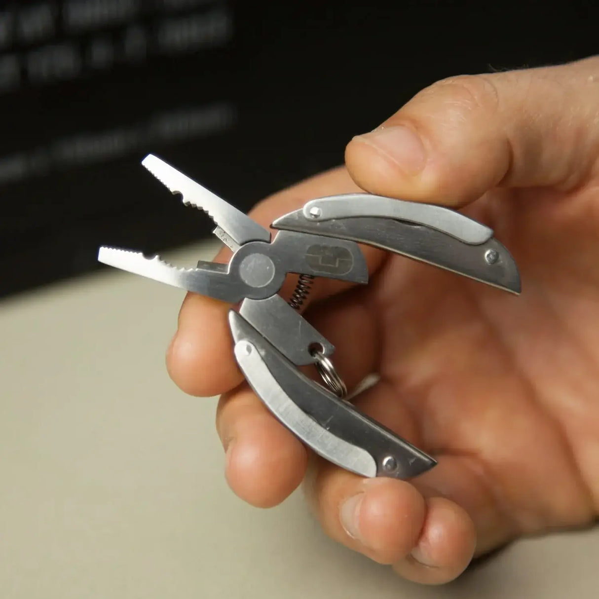 Hand holding True Utility Scarab 7-in-1 compact multi tool with plier function.