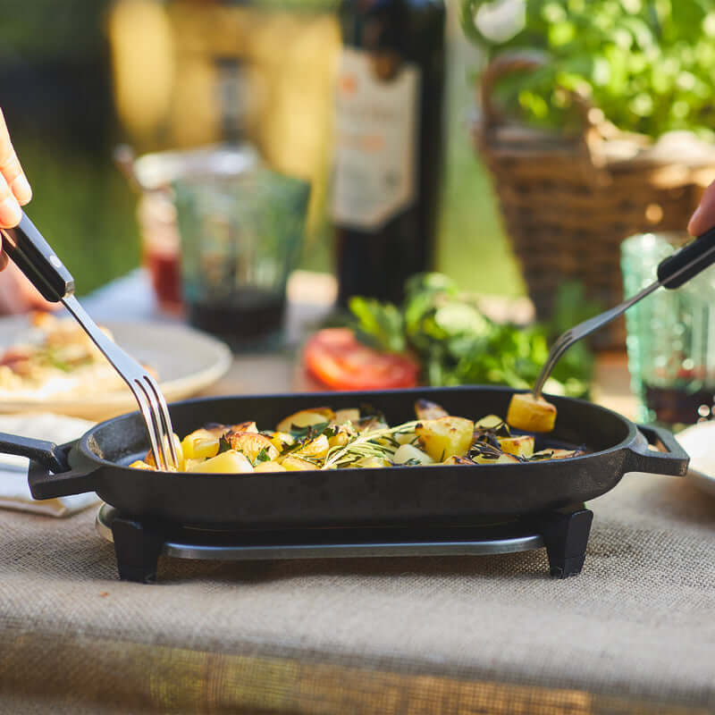 Ooni Cast Iron Sizzler Pan used for cooking vegetables outdoors, showcasing its utility in outdoor cooking and dining experiences.