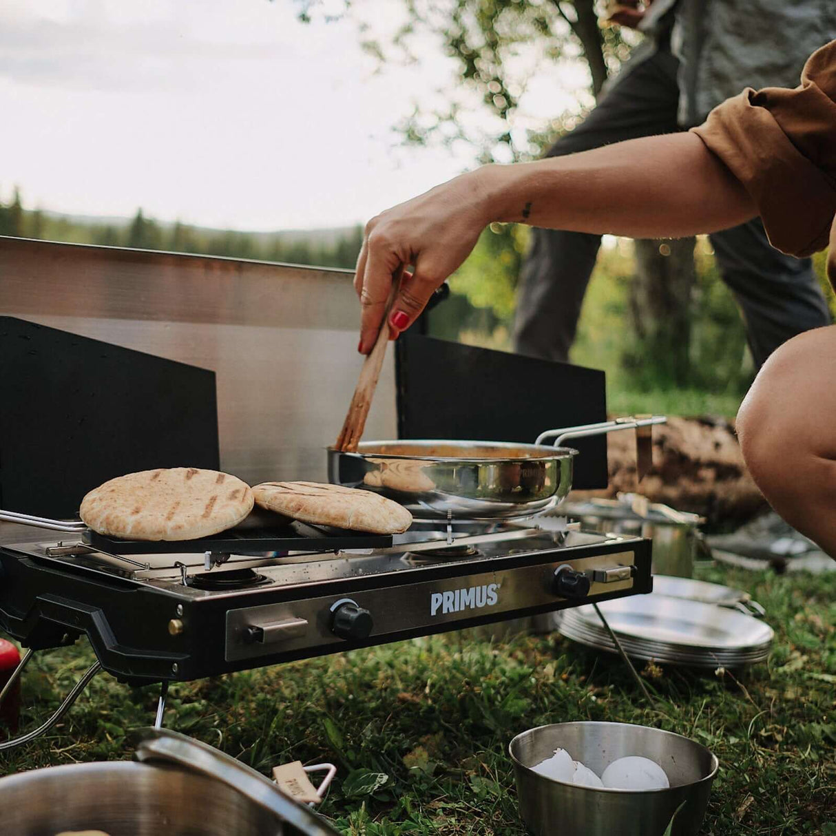 Cooking outdoors with Primus Tupike Stove II, featuring dual burners, perfect for outdoor culinary adventures and style.