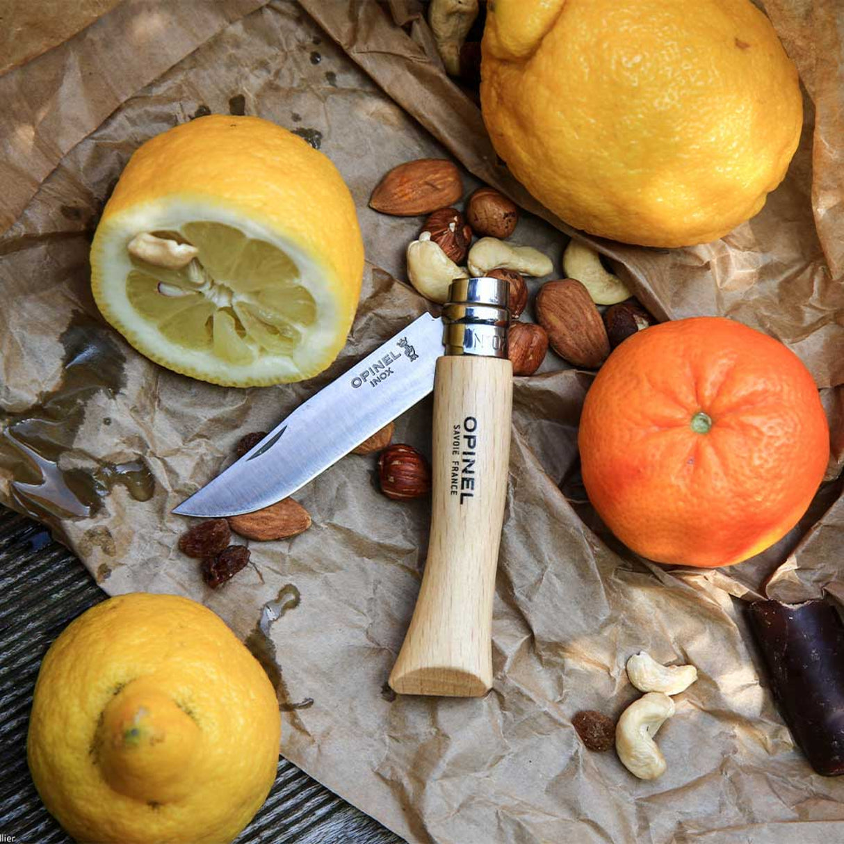 Opinel Traditional Stainless Steel Knife with citrus and nuts on paper, ideal for outdoor activities and daily use.