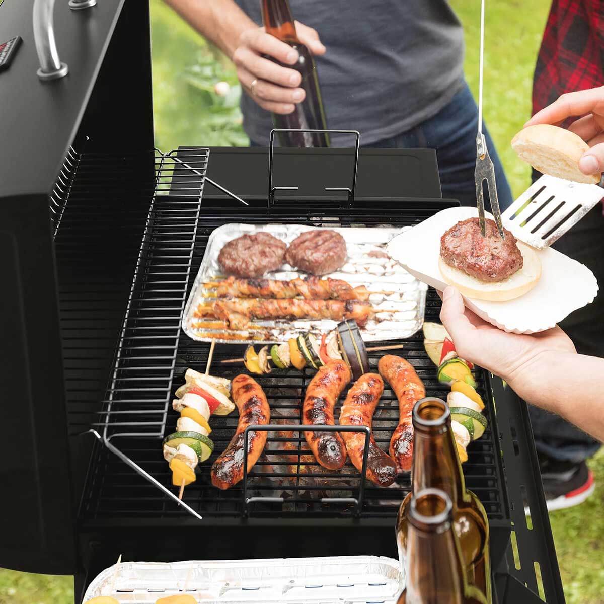 Grilling burgers on the Royal Gourmet 30-Inch Barrel Charcoal Grill with Front Basket at a backyard gathering