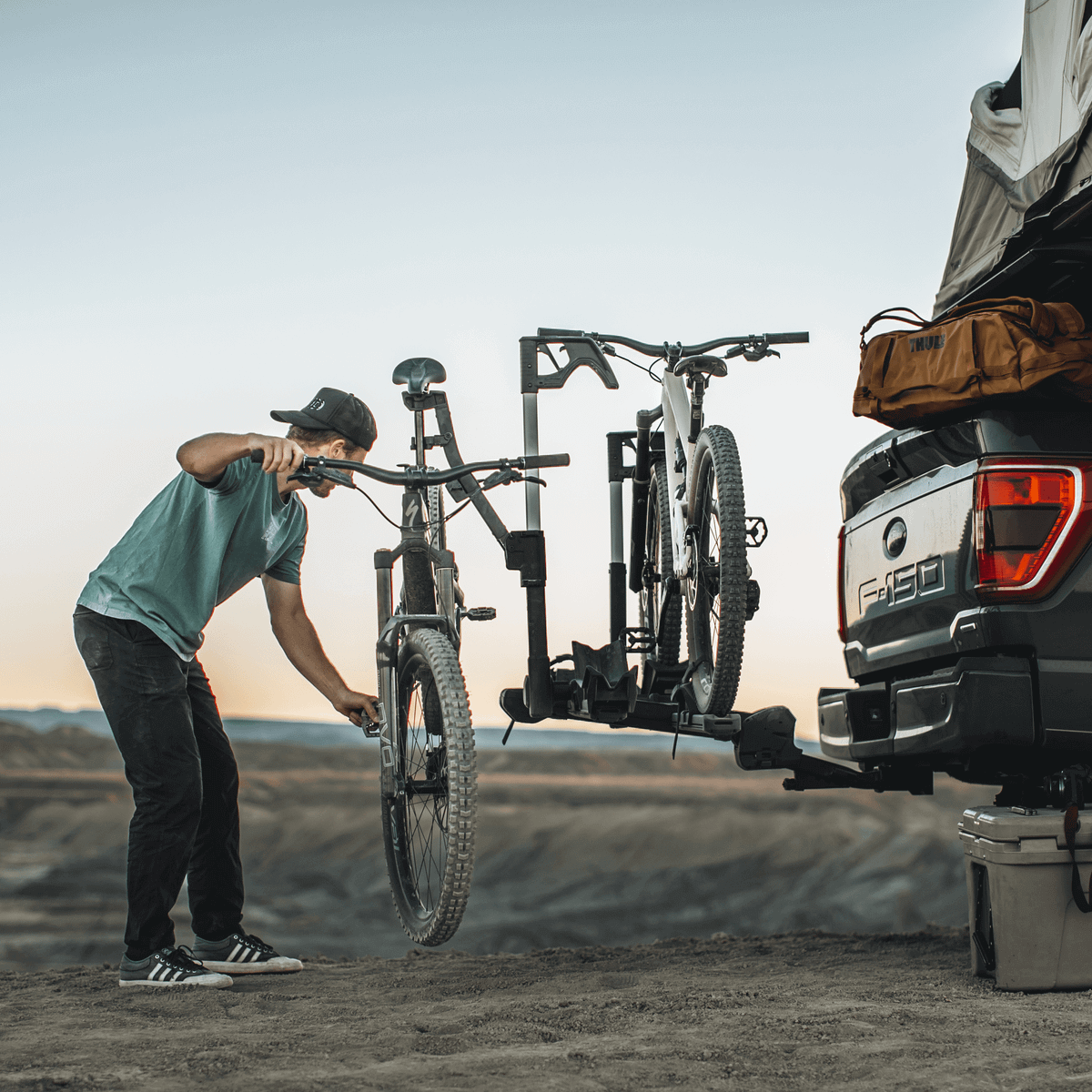 Cyclist using Thule Verse Bike Repair Holder for trailhead adjustments with Thule bike rack on a truck