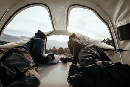 Inside view of Thule Approach - Car Roof Top Tents with two people relaxing; ideal for adventure travel and comfortable outdoor sleeping.