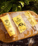 Sun Bum Revitalizing Hair Mask with comb on a wooden surface surrounded by soap bubbles