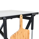 Ooni Folding Table with a stainless steel top and wooden pizza peel attached for easy access during pizza preparation.