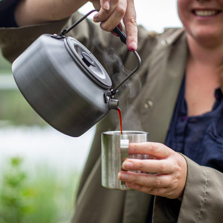 Person pouring from the Primus LiTech Coffee and Tea Kettle into a metal cup outdoors.