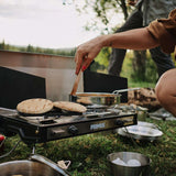 Cooking outdoors with Primus Tupike Stove II, featuring dual burners, perfect for outdoor culinary adventures and style.