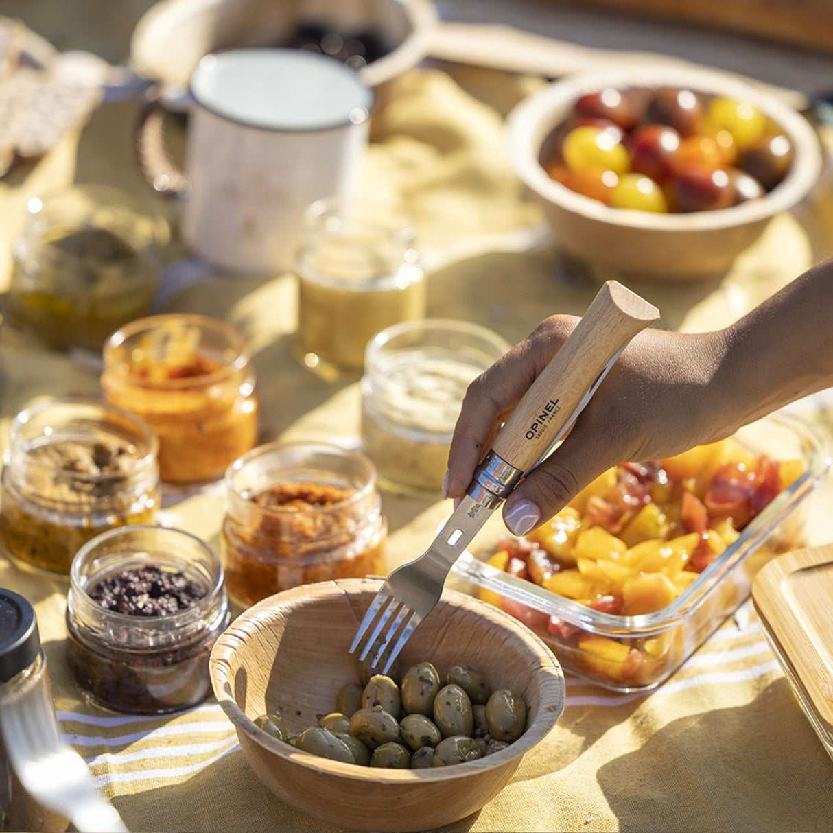 Using Opinel Complete Picnic + Set fork during outdoor meal setup, showcasing sustainable dining accessories on a picnic table.