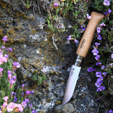Opinel Traditional Stainless Steel Knife with wooden handle in a natural outdoor setting surrounded by purple flowers.